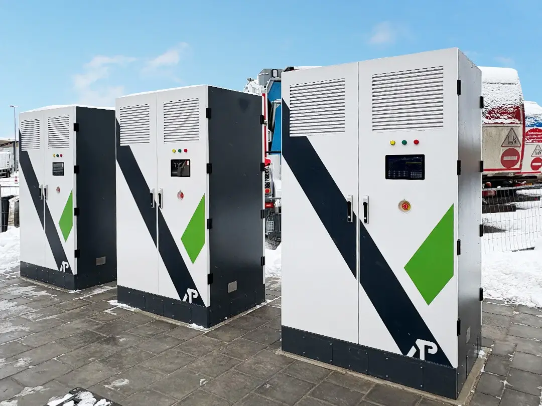 Drie moderne witte laadstations met zwarte en groene accenten staan opgesteld in de sneeuw.